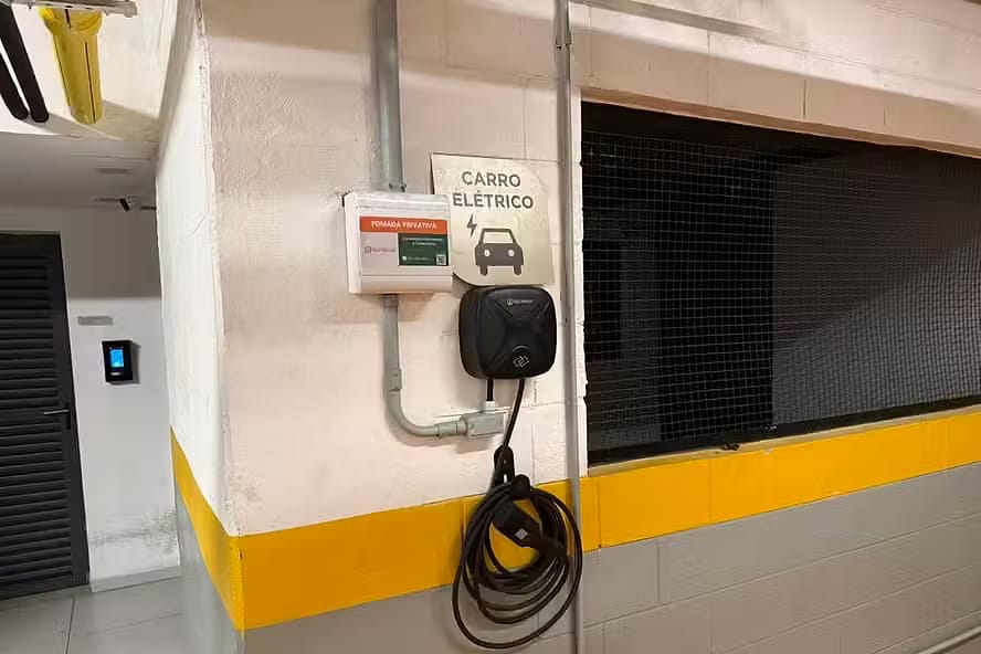 Carregador de carro elétrico (wallbox) instalado na garagem de um prédio, com placa de vaga para carro elétrico